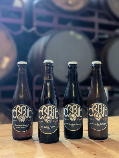 Four bottles of Barrel-aged diggers series Orbit beers on a wooden surface with barrels in the background