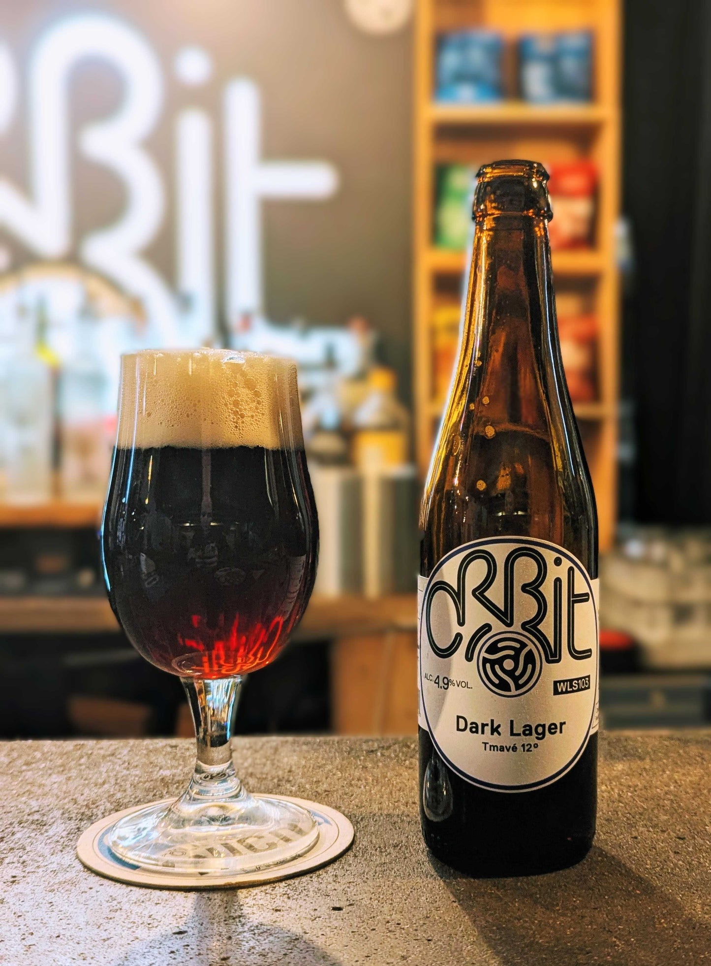 Orbit Dark Lager bottle and glass on a bar counter with 'Orbit' branding in the background.